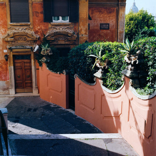 Sun shines through buildings on pastel colored wall and steps in Rome