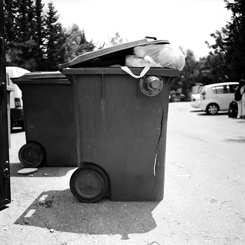 Black and white square photo of trashcan