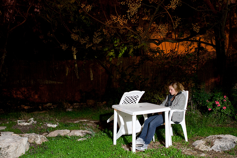 Young woman sits alone on plastic white chairs next to table