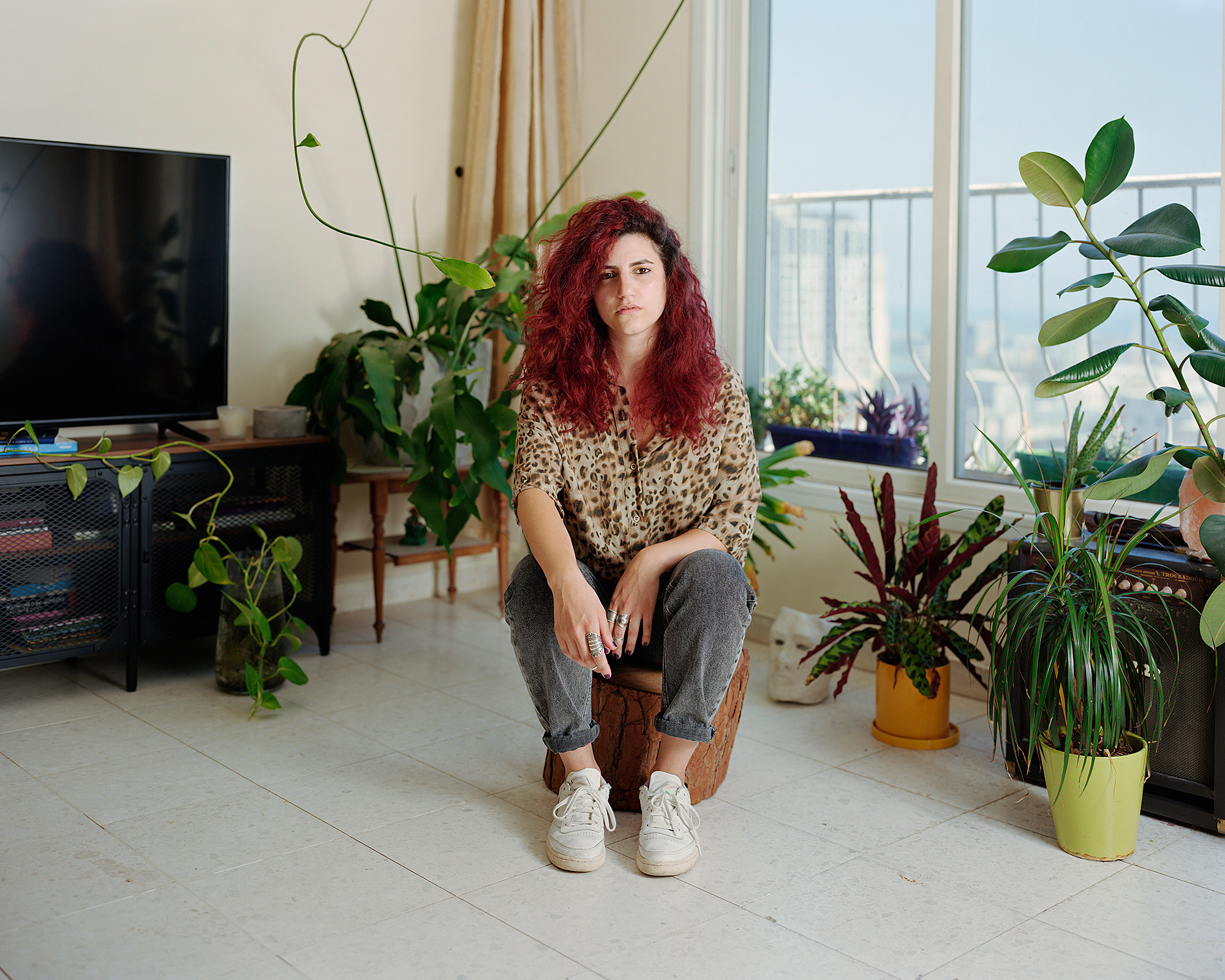 Young woman sitting on tree stump in living room surrounded by plants