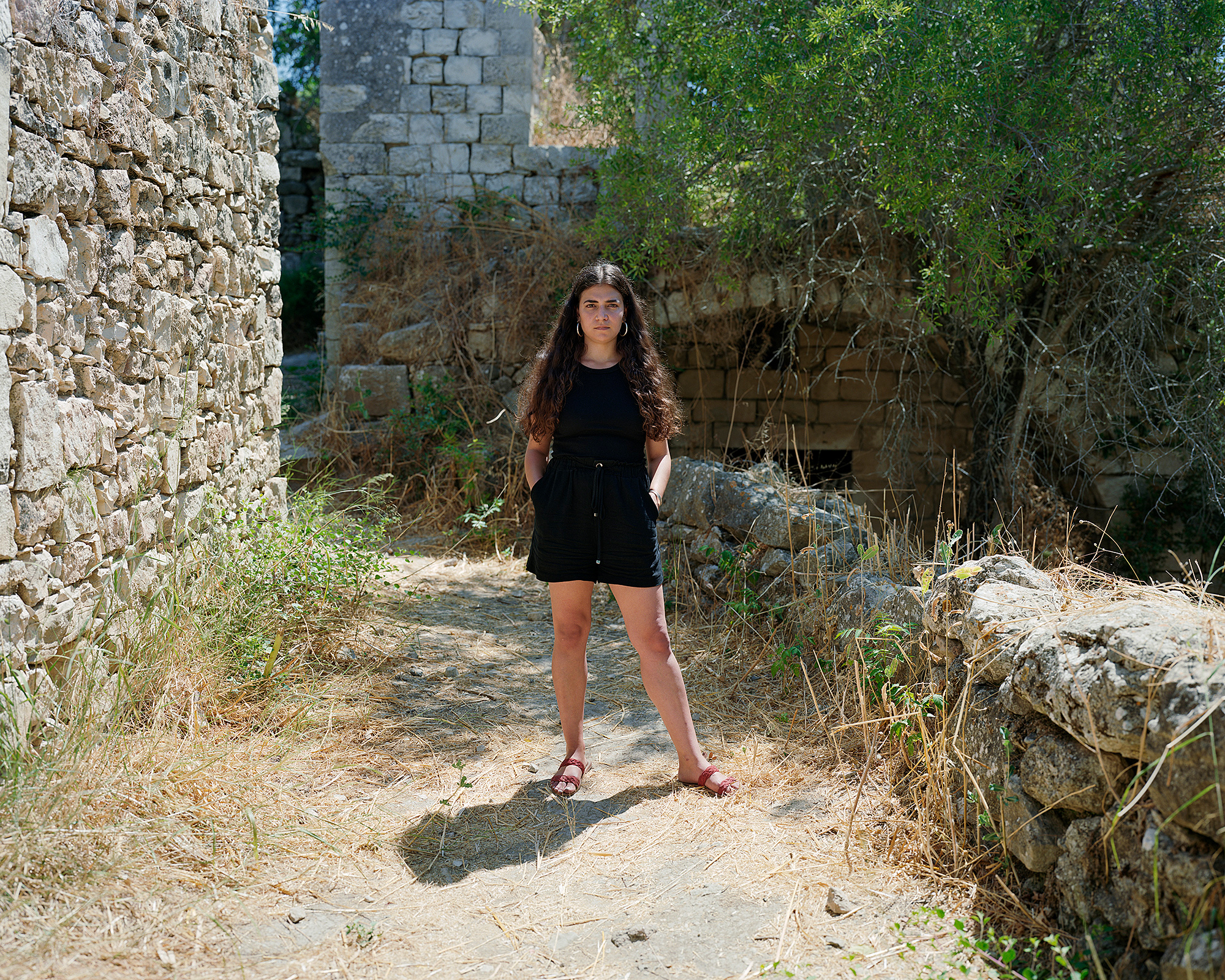 Young woman standing on dirt path among abandoned stone houses